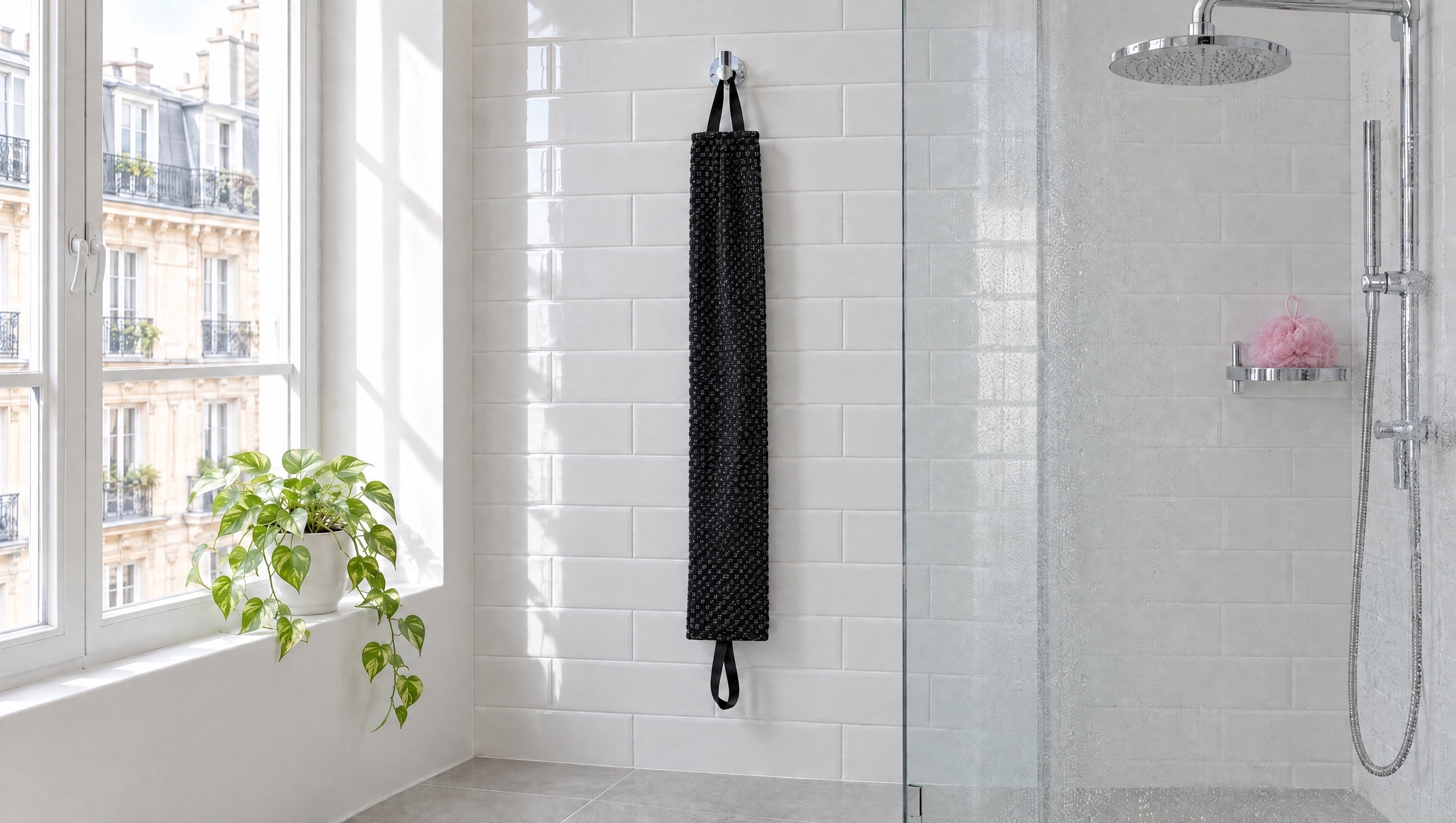 Une douche à l’italienne en carrelage blanc ; à côté, la serviette Seshin noire pend à une patère, une poignée à chaque bout.