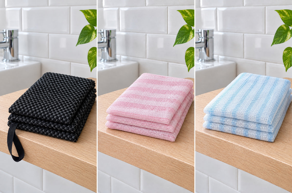 Les trois coloris de la serviette Seshin, chacun plié sur la même tablette en chêne : noir avec sa poignée, rose rayé et bleu rayé.