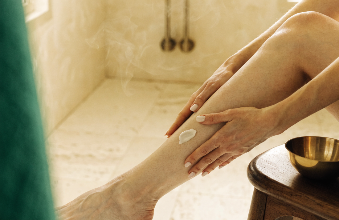 Deux mains appliquent de la crème sur une jambe, au bord d’un bain.