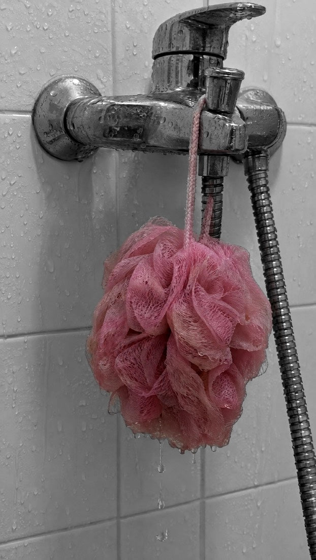 Une fleur de douche rose, mouillée, pend au robinet et goutte.